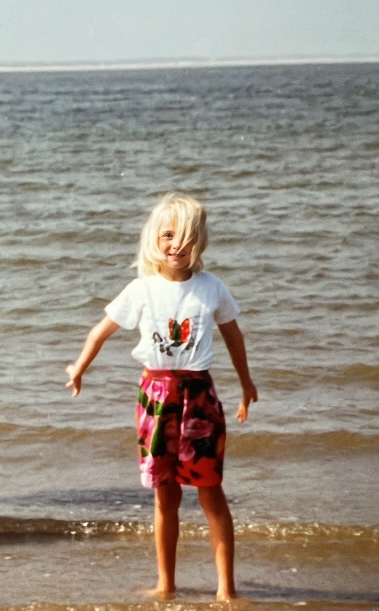 Une fille de 7 ans a le dos vers la mer et regarde la caméra